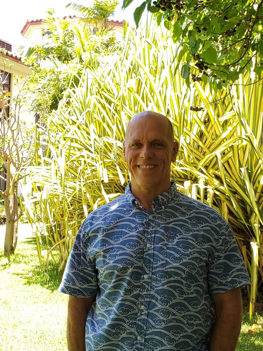 Steve wearing a blue and white aloha shirt standing in front of a large green and yellow tree